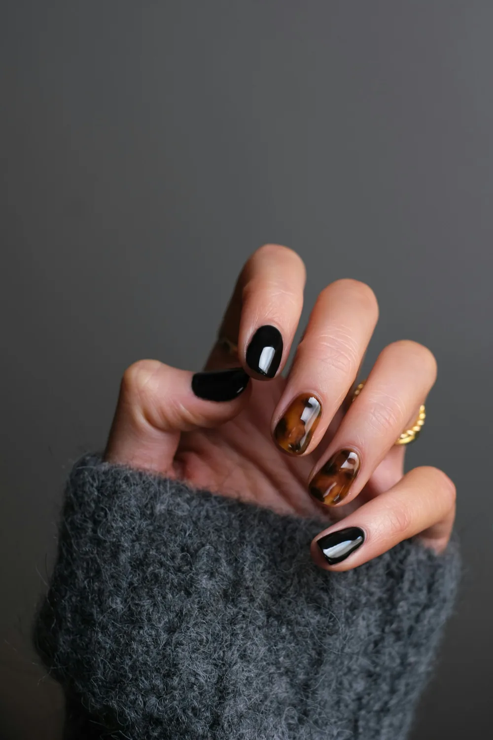 Mano con uñas negras y de efecto carey, con un anillo dorado