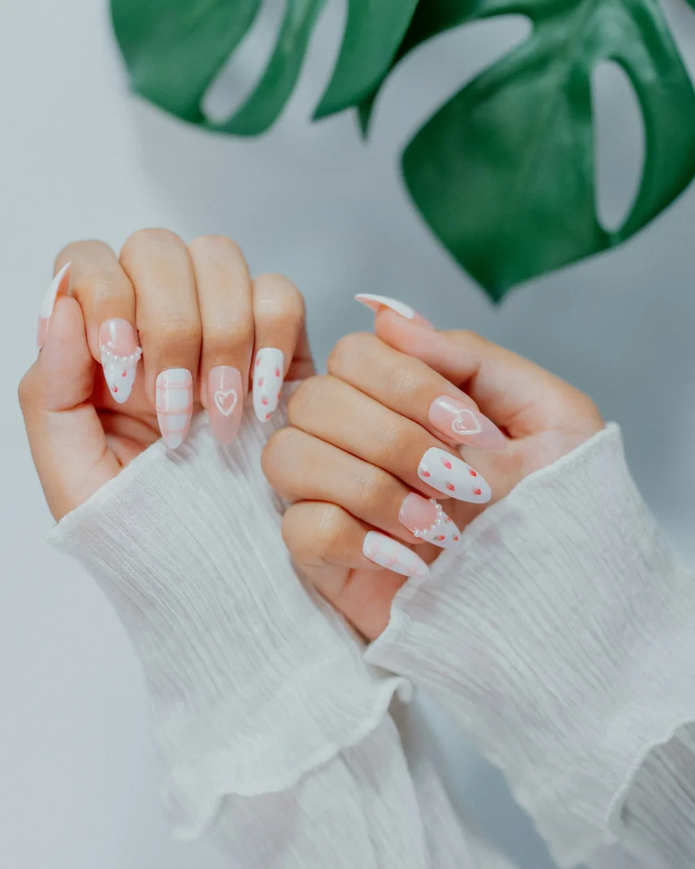 Manos con uñas blancas y rosas decoradas con pequeños corazones