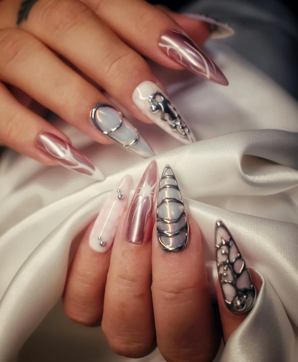 Uñas stiletto largas en cromo rosado con relieves plateados y piedras