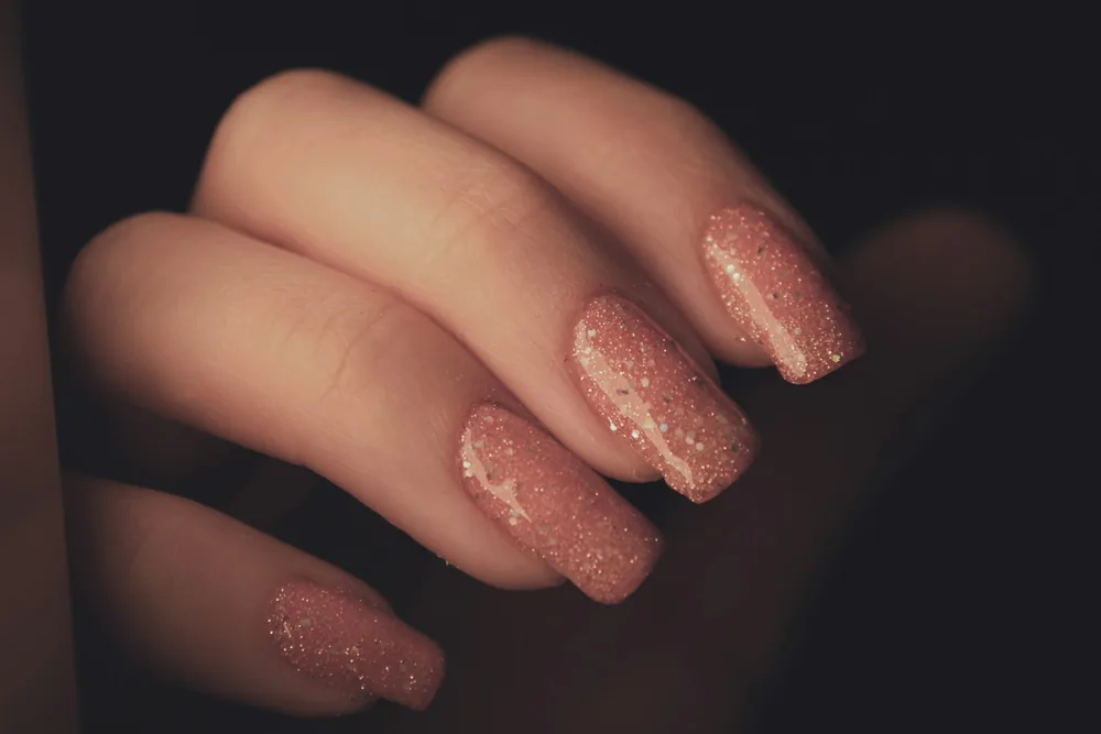 Uñas cuadradas con purpurina rosa dorada sobre fondo oscuro